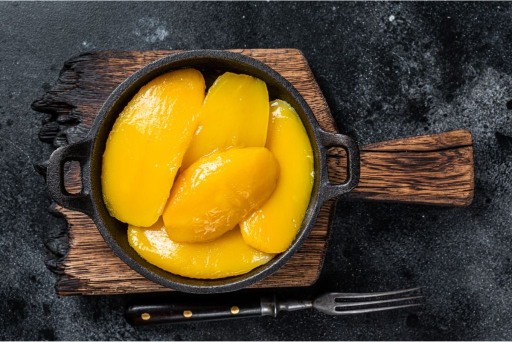 Canned mango slices in cast-iron skillet on cutting board
