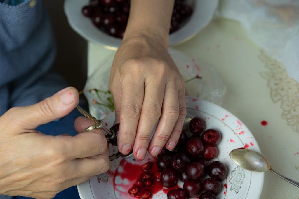 Woman expelling pits from cherries using a tool, holding it over a bowl