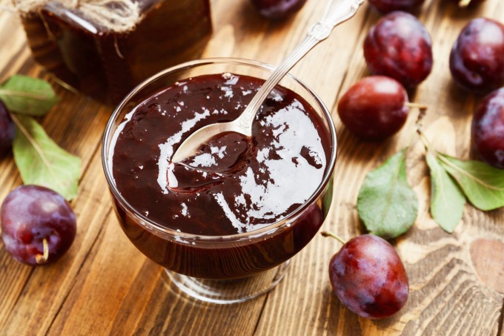 Bowl of plum jam surrounded by fresh plums