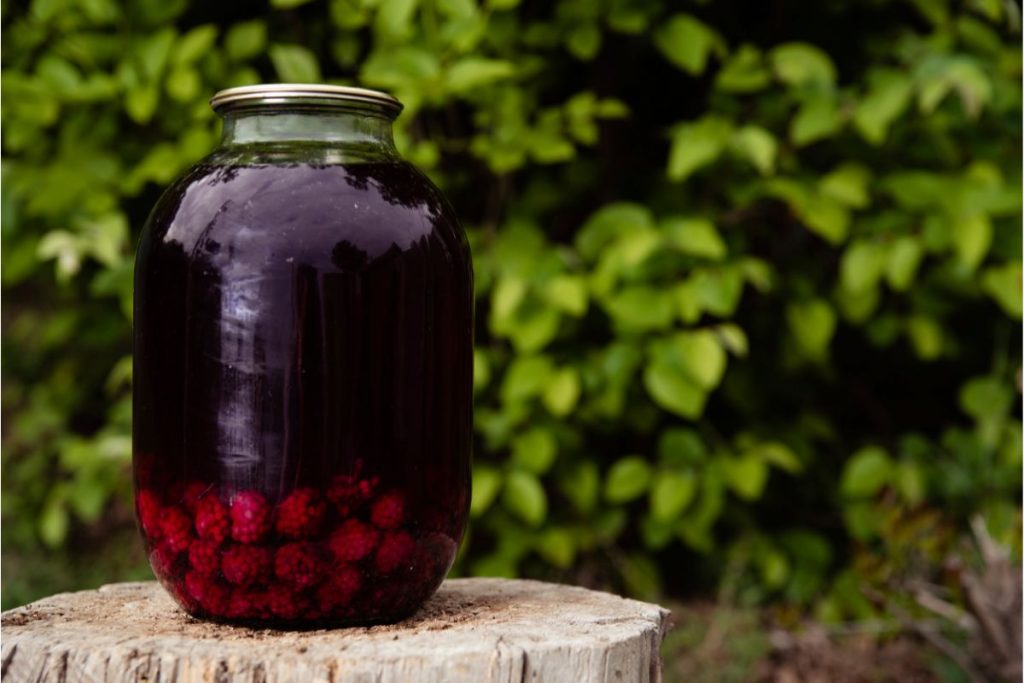 Gallon glass jar of raspberries with fruit juice